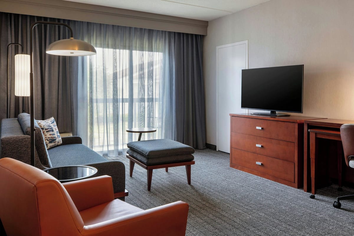 Ein Hotelzimmer mit Sofa, Hocker, Fernseher, Schreibtisch und Lampe.