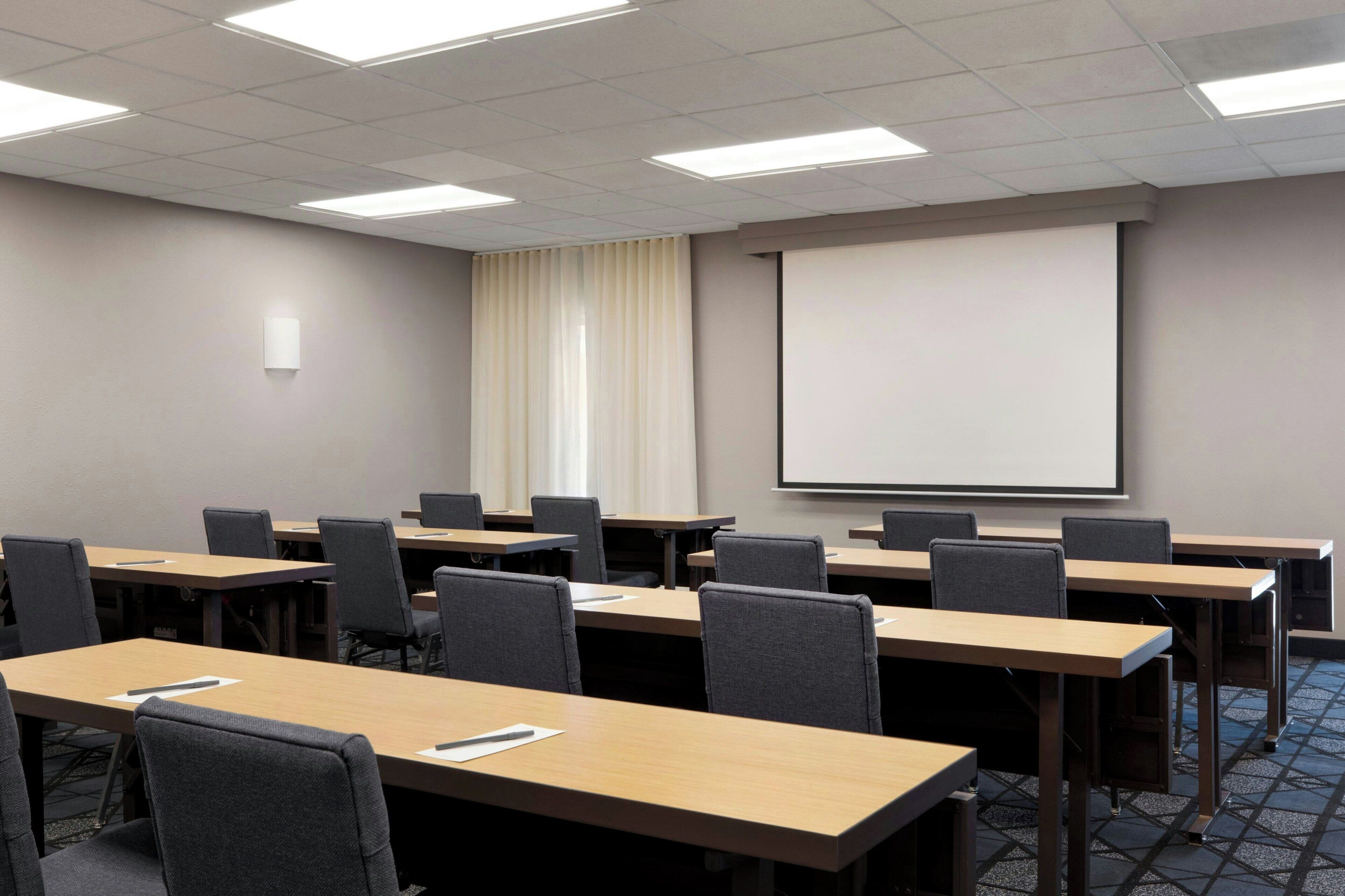 A conference room with multiple tables and chairs, a projector screen, and a whiteboard.