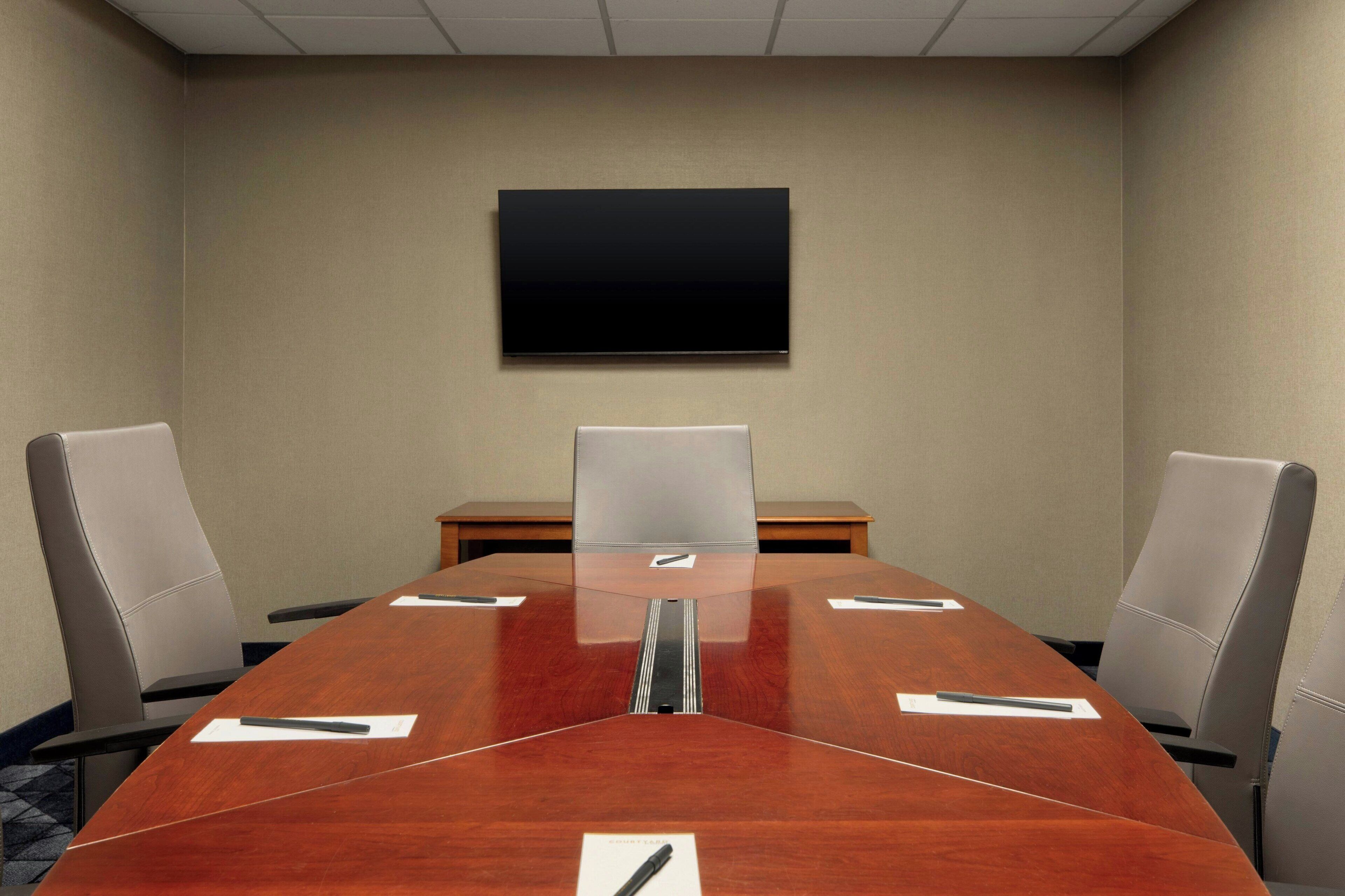 Un salón de conferencias con una mesa larga, cuatro sillas, un televisor de pantalla plana en la pared y una mesa de madera.
