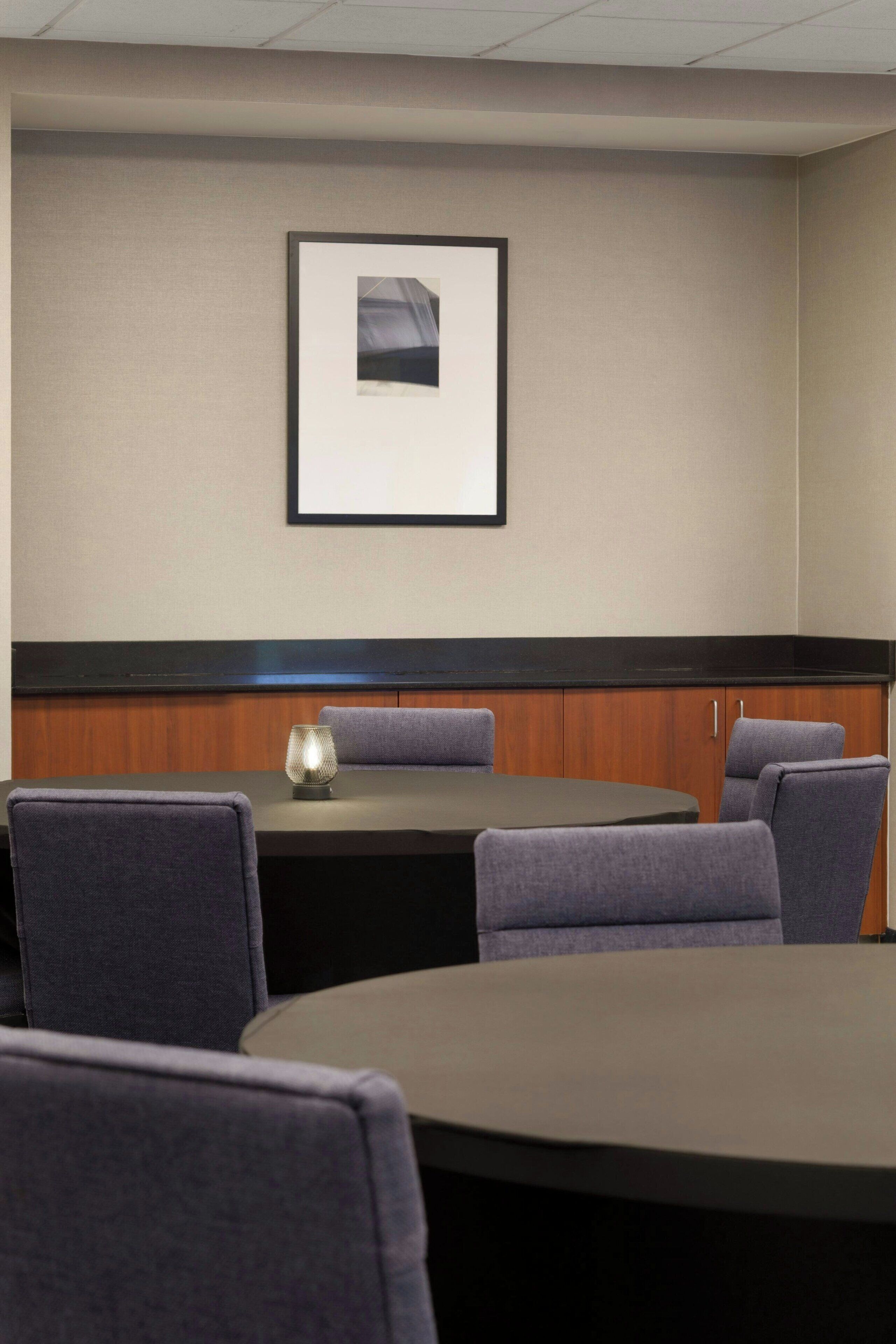 Uma sala de conferências com uma mesa redonda, quatro cadeiras, um quadro na parede e um painel de madeira sob a mesa.