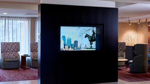 A modern lobby with a large digital screen displaying a cityscape, comfortable seating, and a red carpet. - Sonesta Select Kansas City Airport Tiffany Springs (Kansas City)