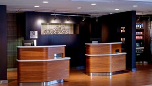A reception area with two wooden reception desks, a wall-mounted artwork, and a shelf with bottled water. - Sonesta Select Kansas City Airport Tiffany Springs (Kansas City)