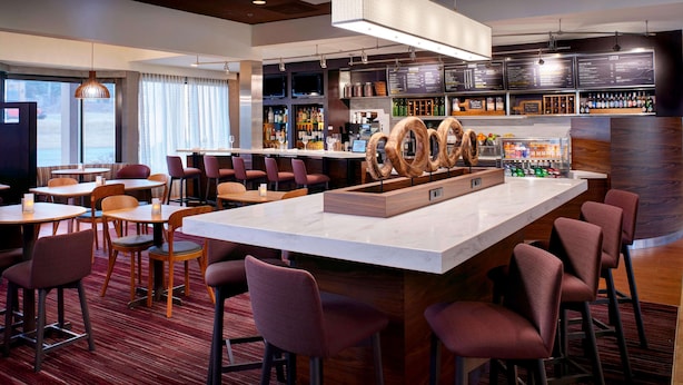 A modern bar area with a marble counter, multiple seating options, and a variety of bottles and glasses on shelves. - Sonesta Select Kansas City Airport Tiffany Springs (Kansas City)
