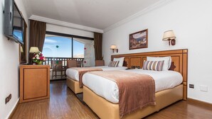 Habitación de hotel con dos camas, un televisor, un balcón con vistas y suelo de madera.