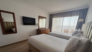 Habitación de hotel con dos camas, televisión, espejo, cómoda y ventana con cortinas.