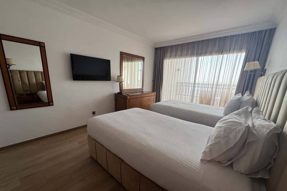 A hotel room with two beds, a TV, a mirror, a dresser, and a window with curtains.