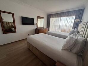 A hotel room with two beds, a TV, a mirror, a dresser, and a window with curtains.