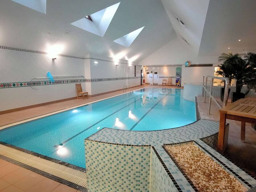 Ein Hallenbad mit gefliestem Boden, einer Holzbank und einem Stuhl.