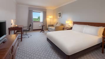 Quarto de hotel com uma cama grande, uma escrivaninha com cadeira, um sofá, uma televisão e uma janela com cortinas.