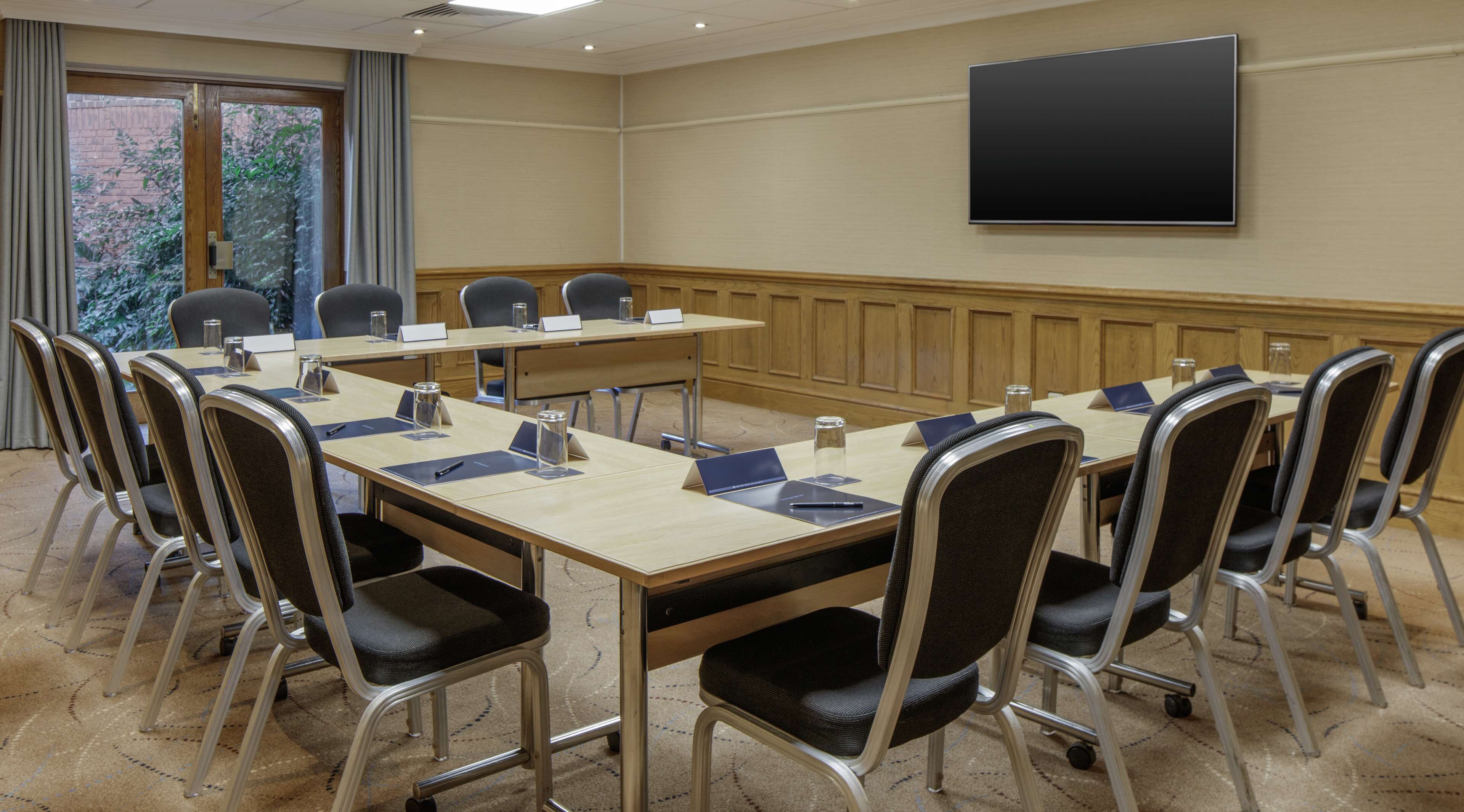 A conference room with a large table, chairs, a projector screen, and a view of greenery outside.