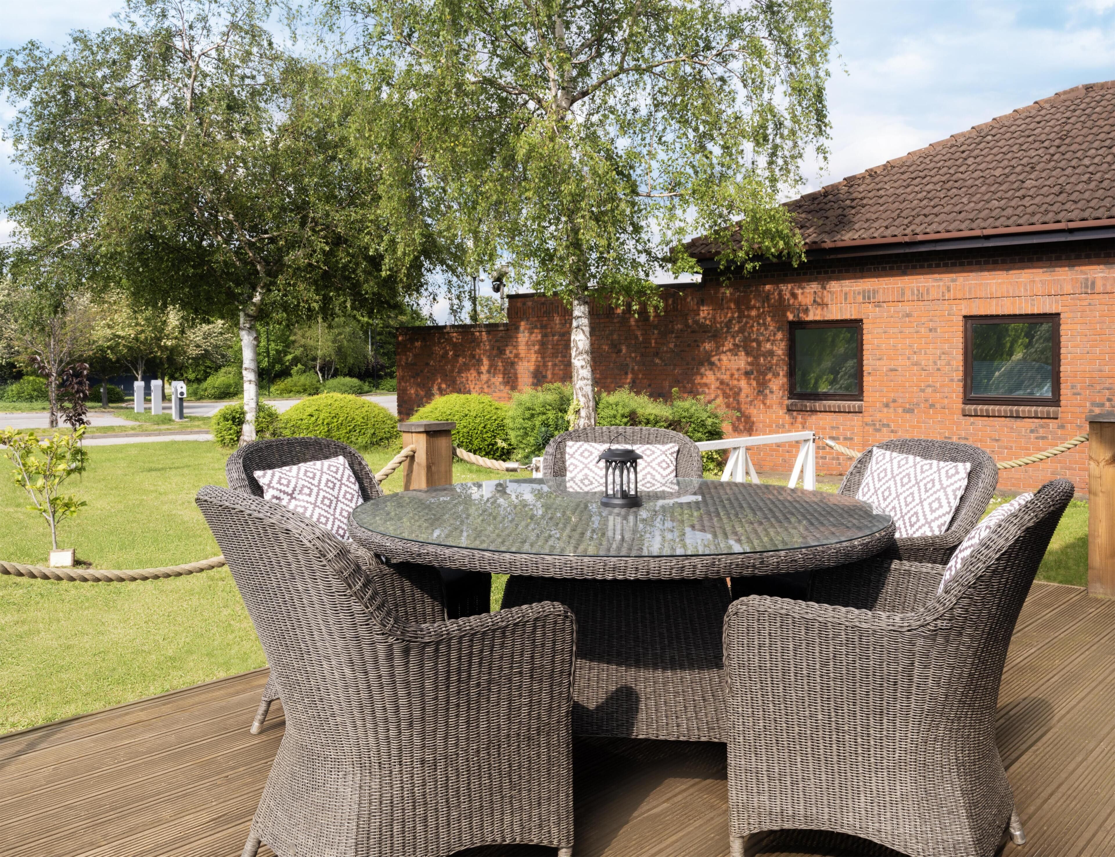Une terrasse extérieure avec des meubles en osier, une table ronde et, en arrière-plan, un bâtiment en briques.