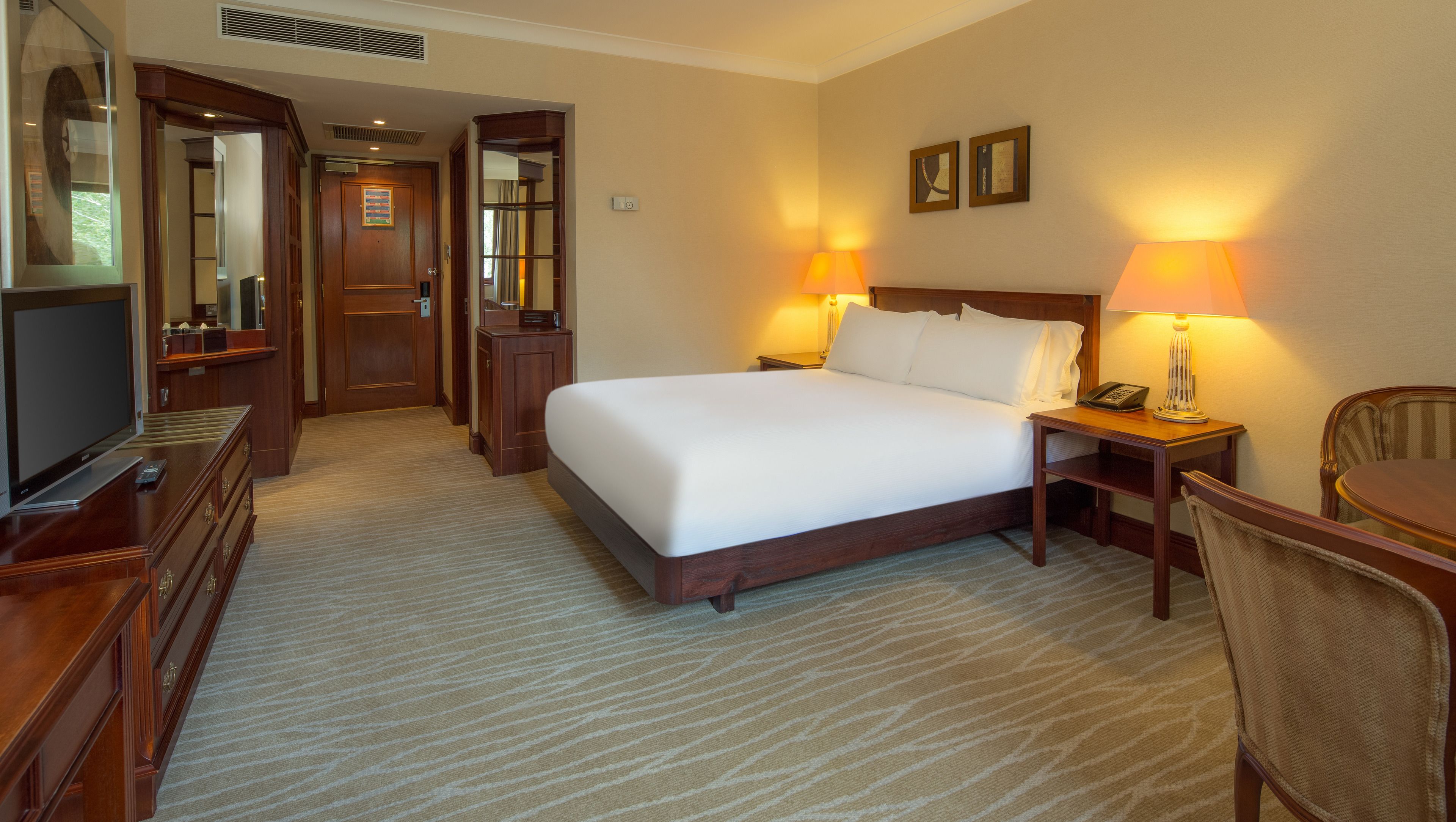A hotel room with a large bed, a desk with a lamp, a chair, a television, and a mirror.