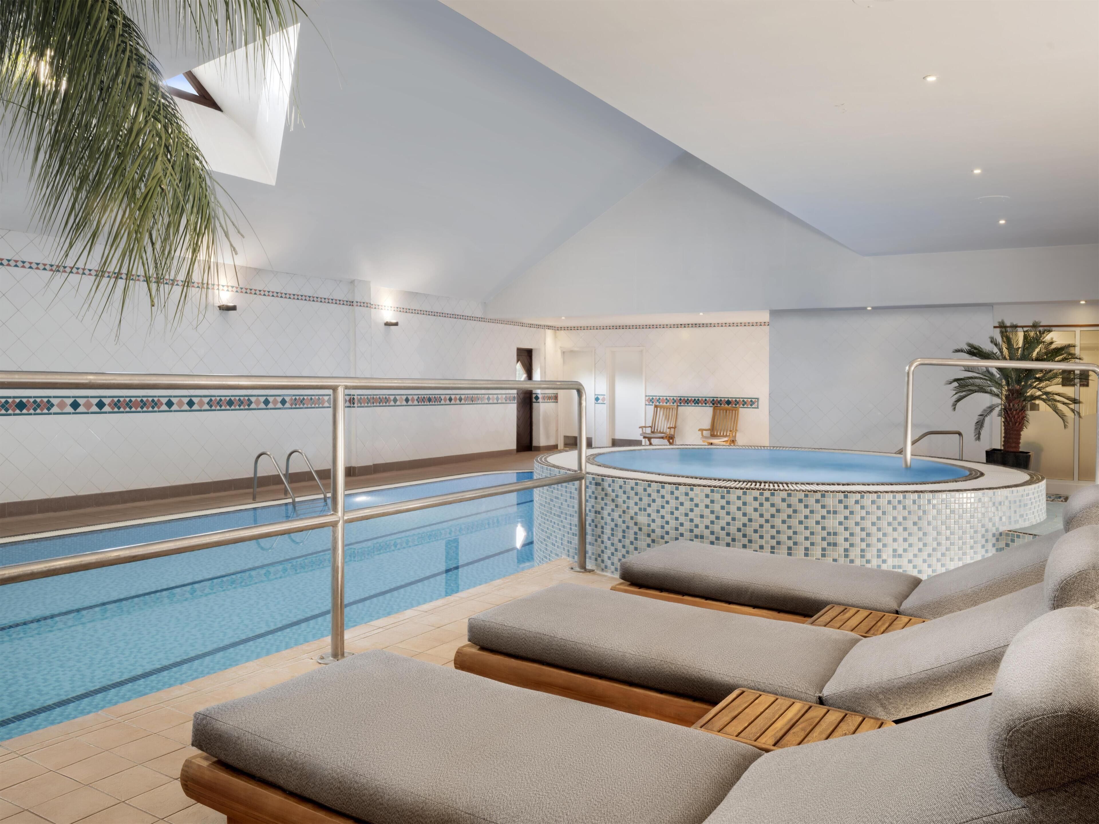 Zona de piscina con un jacuzzi, sillas de descanso y una palmera.