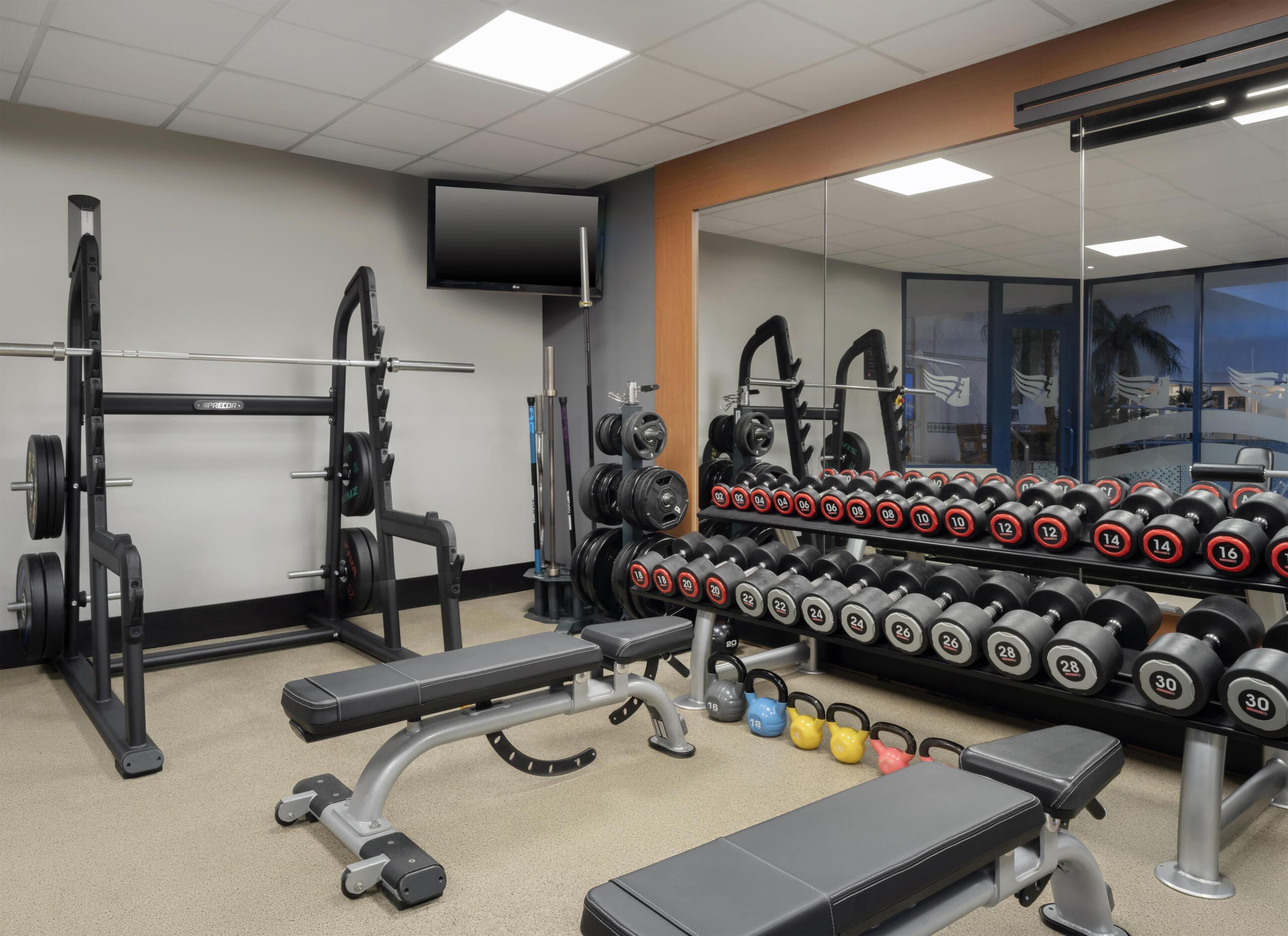 A gym with weightlifting equipment, benches, and a mirrored wall.