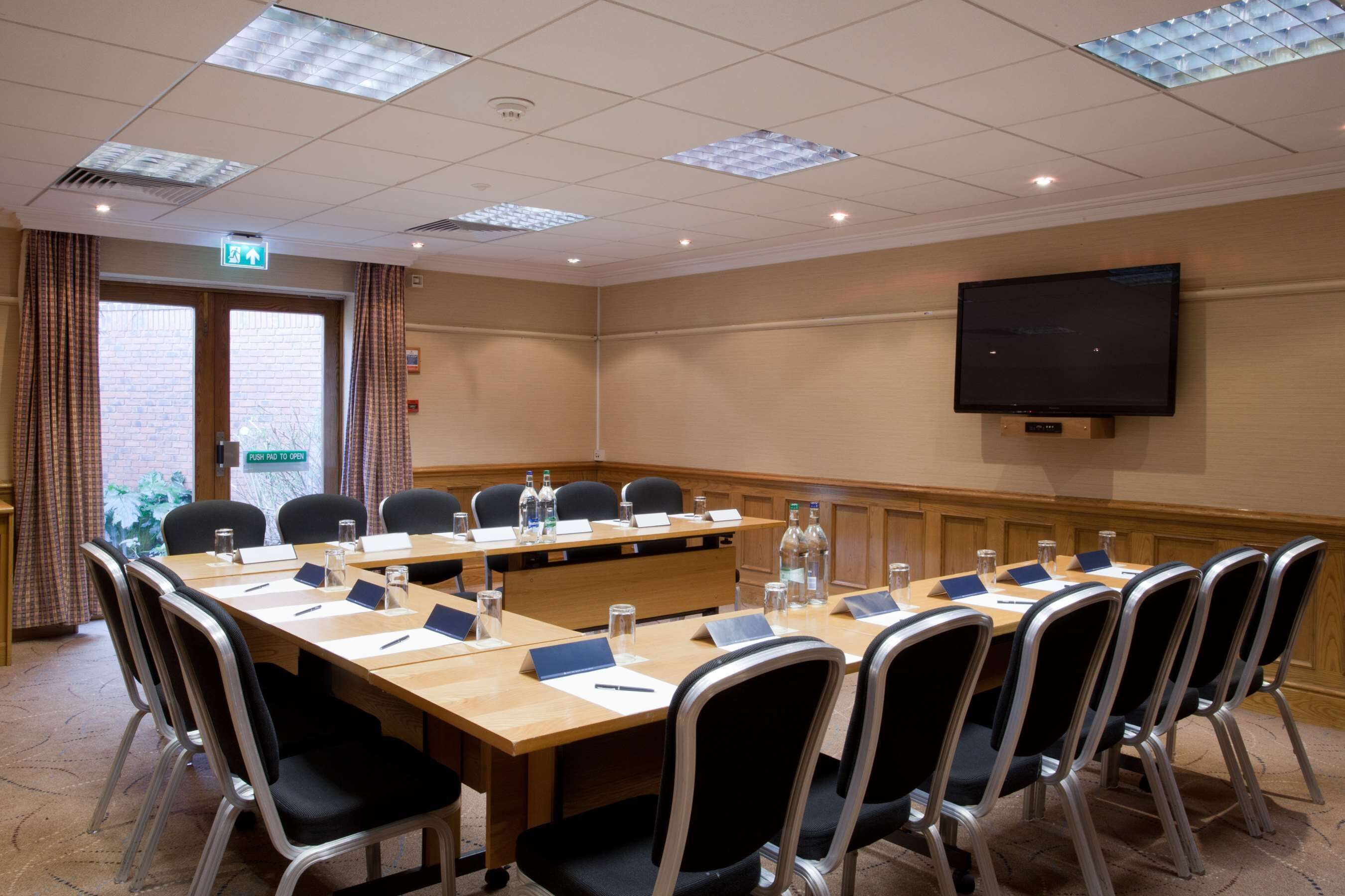 A conference room with a long table, chairs, nameplates, water bottles, and a television on the wall.