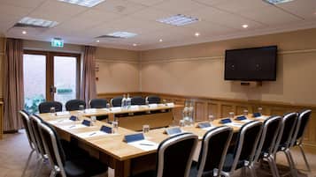 A conference room with a long table, chairs, nameplates, water bottles, and a television on the wall.
