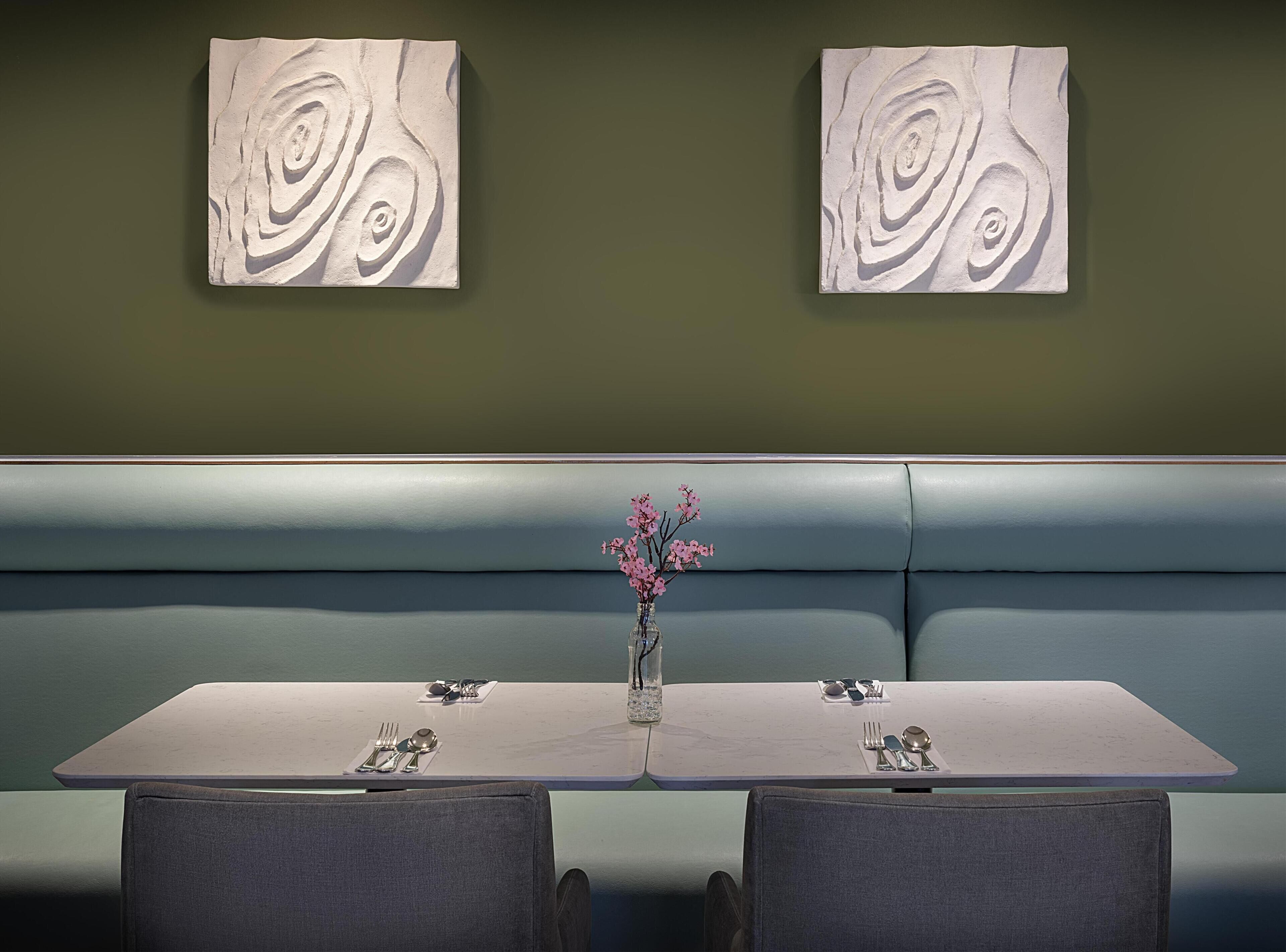 A restaurant with a booth seating area, a table with a vase of flowers, and two abstract wall art pieces.