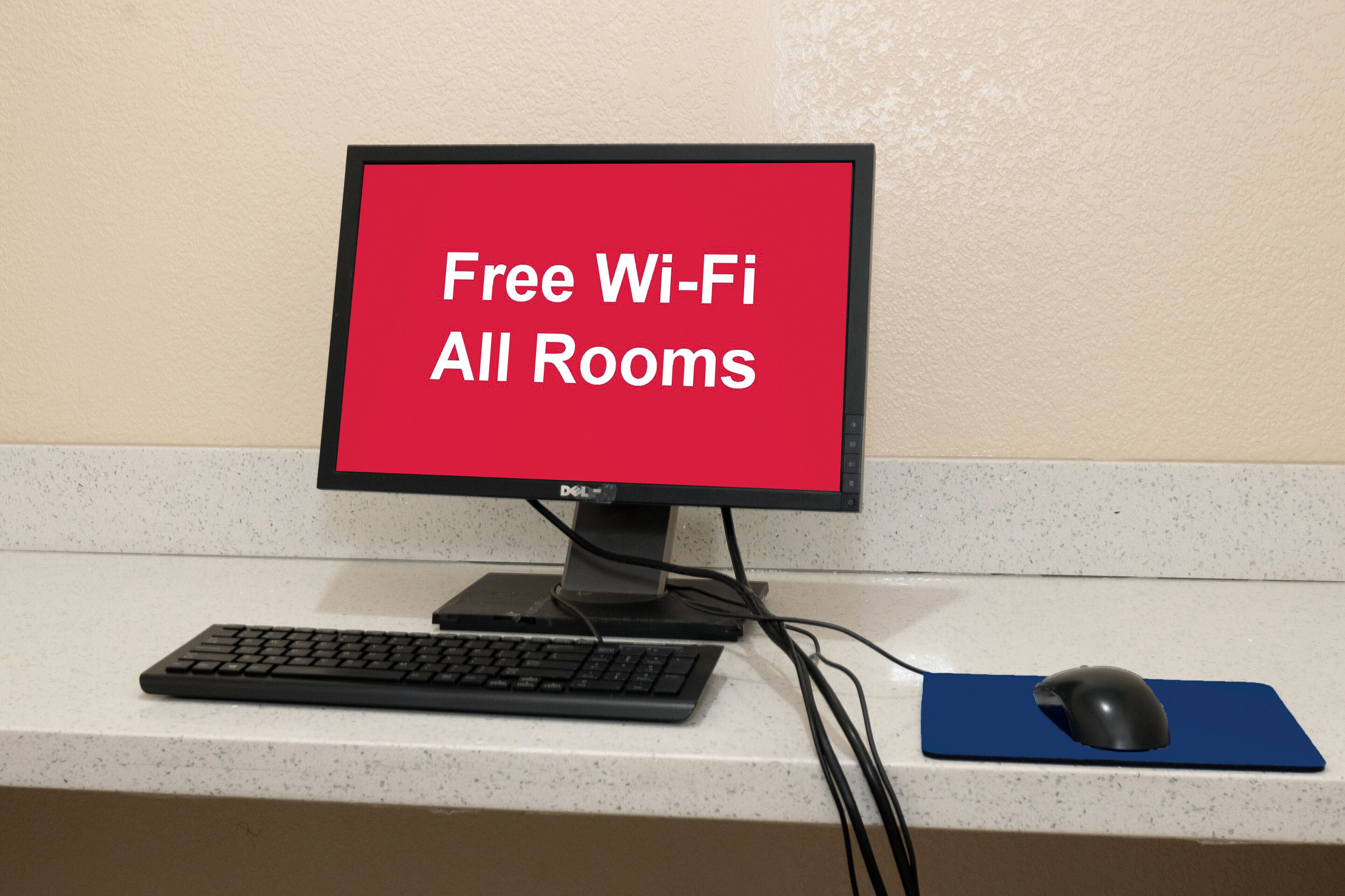 Un monitor de computadora con pantalla roja mostrando 'Free Wi-Fi All Rooms' sobre un escritorio de hotel.