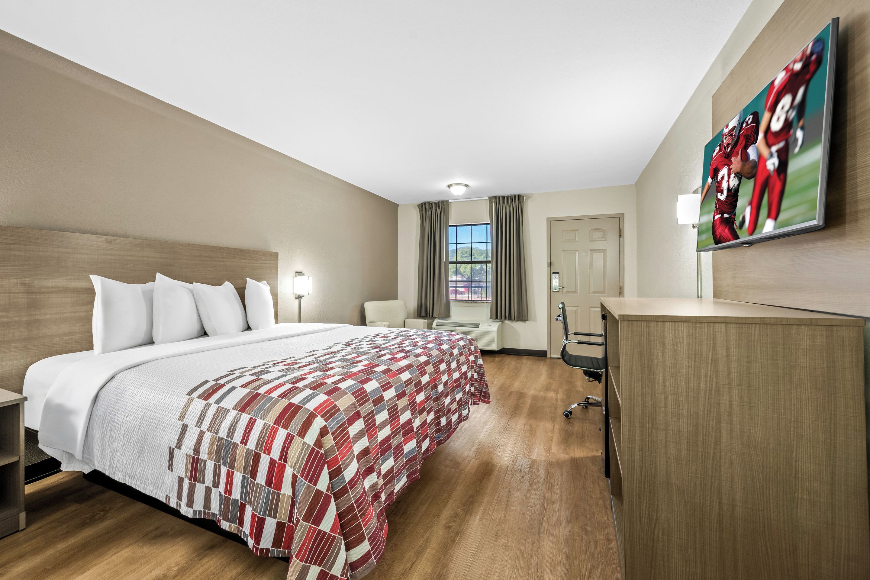 Een hotelkamer met een groot bed, een bureau, een flatscreen televisie en een raam met gordijnen.