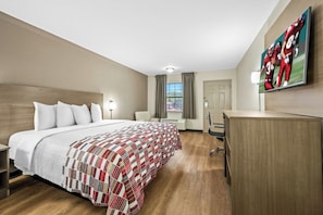 A hotel room with a large bed, a desk, a flat-screen TV, and a window with curtains.