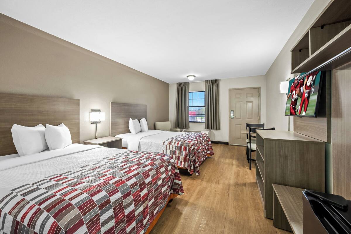 Een hotelkamer met twee bedden, een bureau, een televisie en een raam met gordijnen.