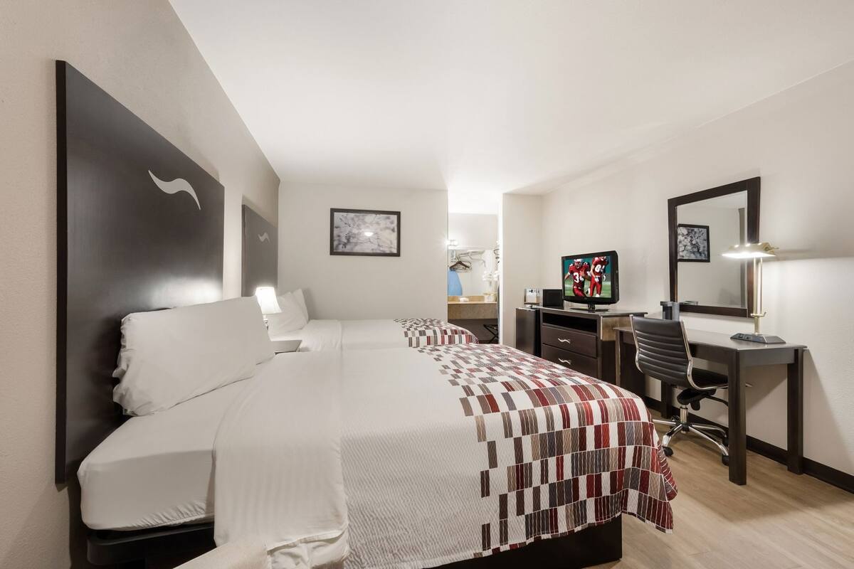 Een hotelkamer met twee bedden, een bureau met stoel, een televisie en een spiegel.