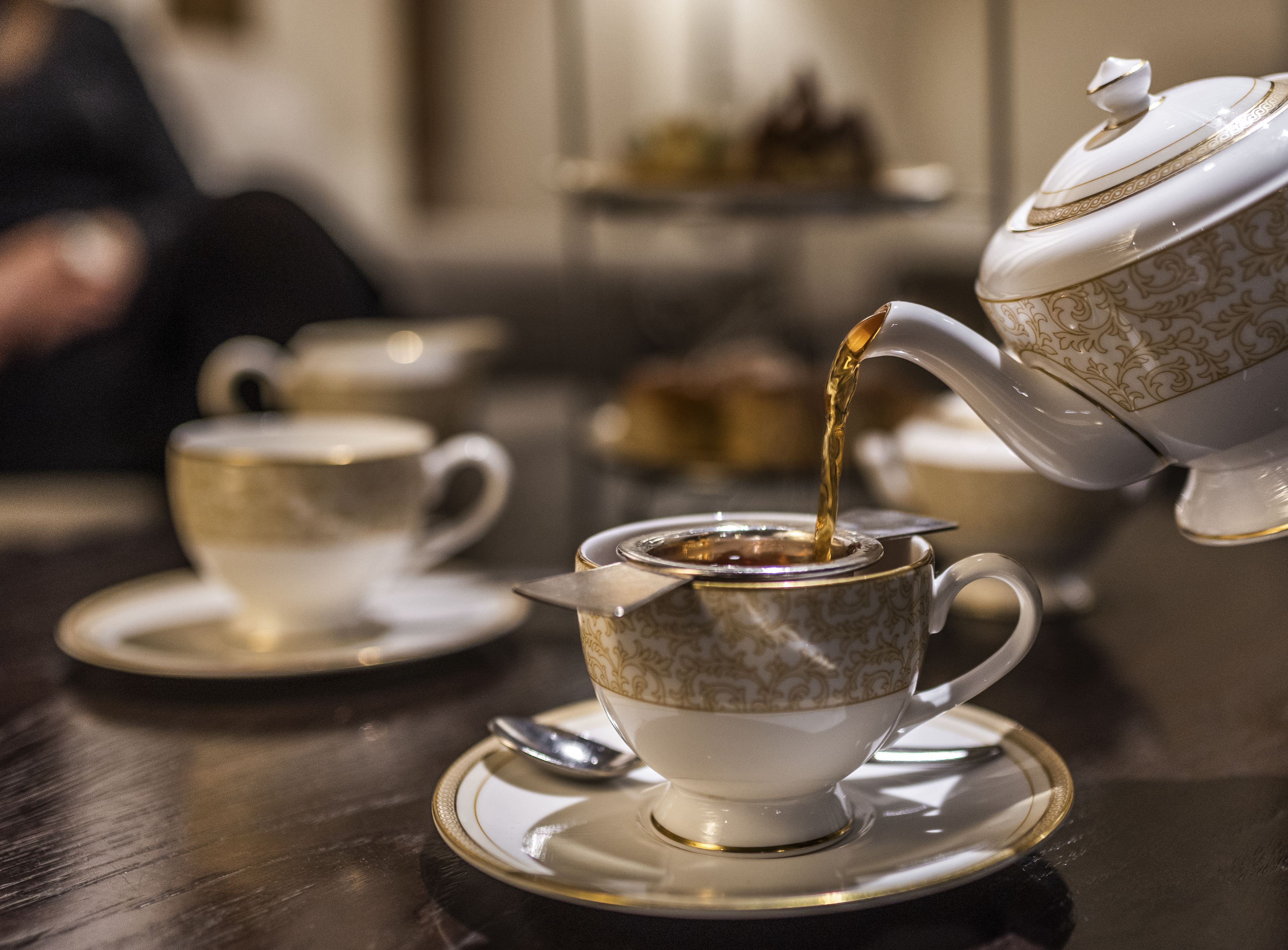 Un juego de té con tetera sirviendo té en una taza, acompañado por un platillo y cuchara.