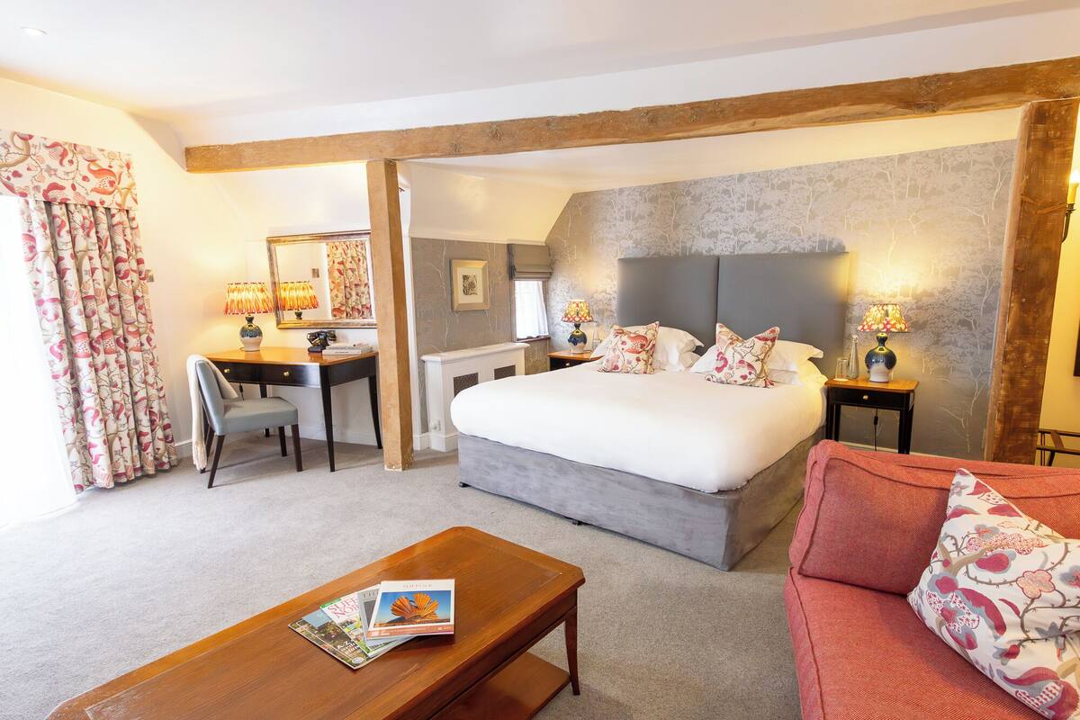 A hotel room with a large bed, a desk, a chair, a sofa, and a coffee table.
