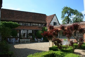 A courtyard with a gravel path, a wooden bench, and white metal chairs. - The Swan Hotel (Sudbury)