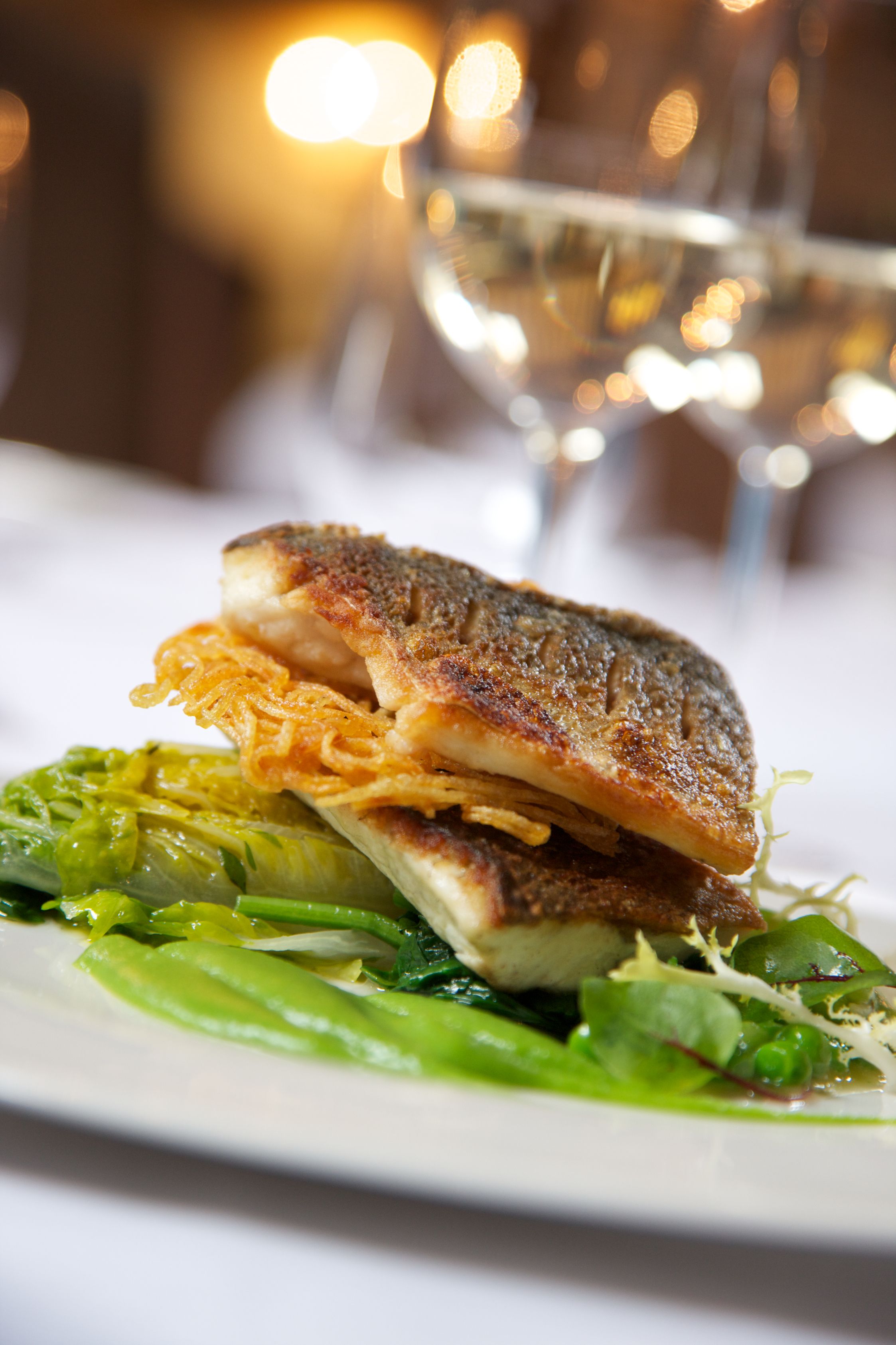 A plate with a grilled fish sandwich and greens.