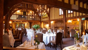 A dining area with multiple tables set for a meal, wooden beams on the ceiling, and a brick wall in the background. - The Swan Hotel (Sudbury)