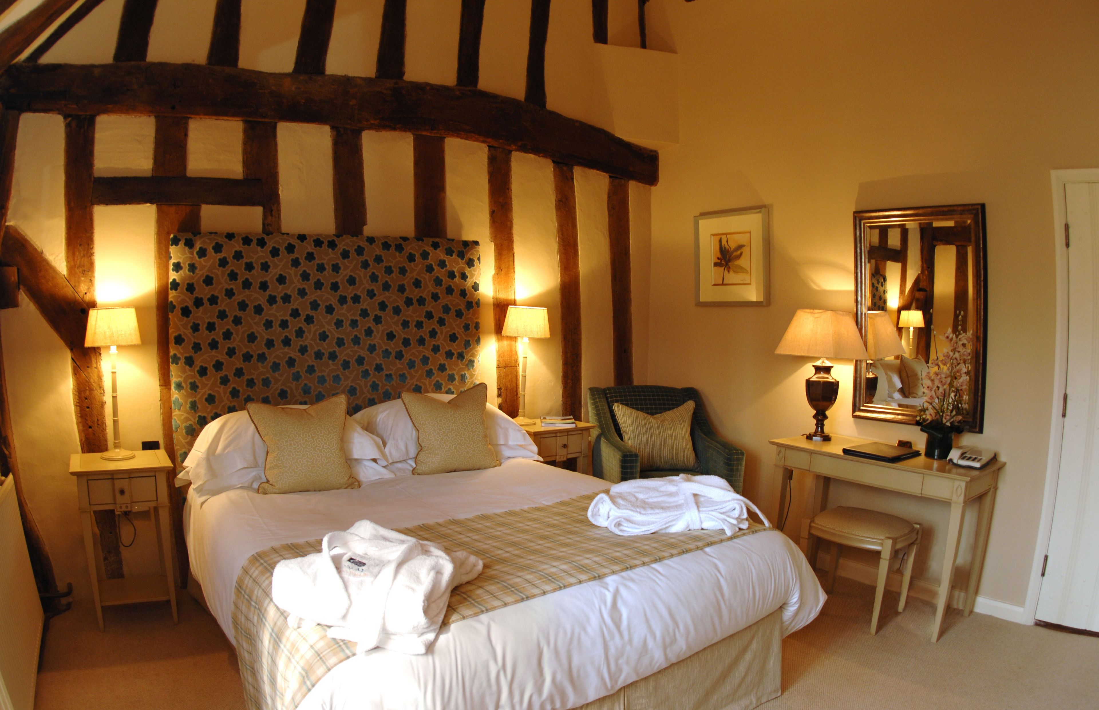 Habitación de hotel con una cama grande, dos mesitas de noche con lámparas, un escritorio con una silla y un espejo.