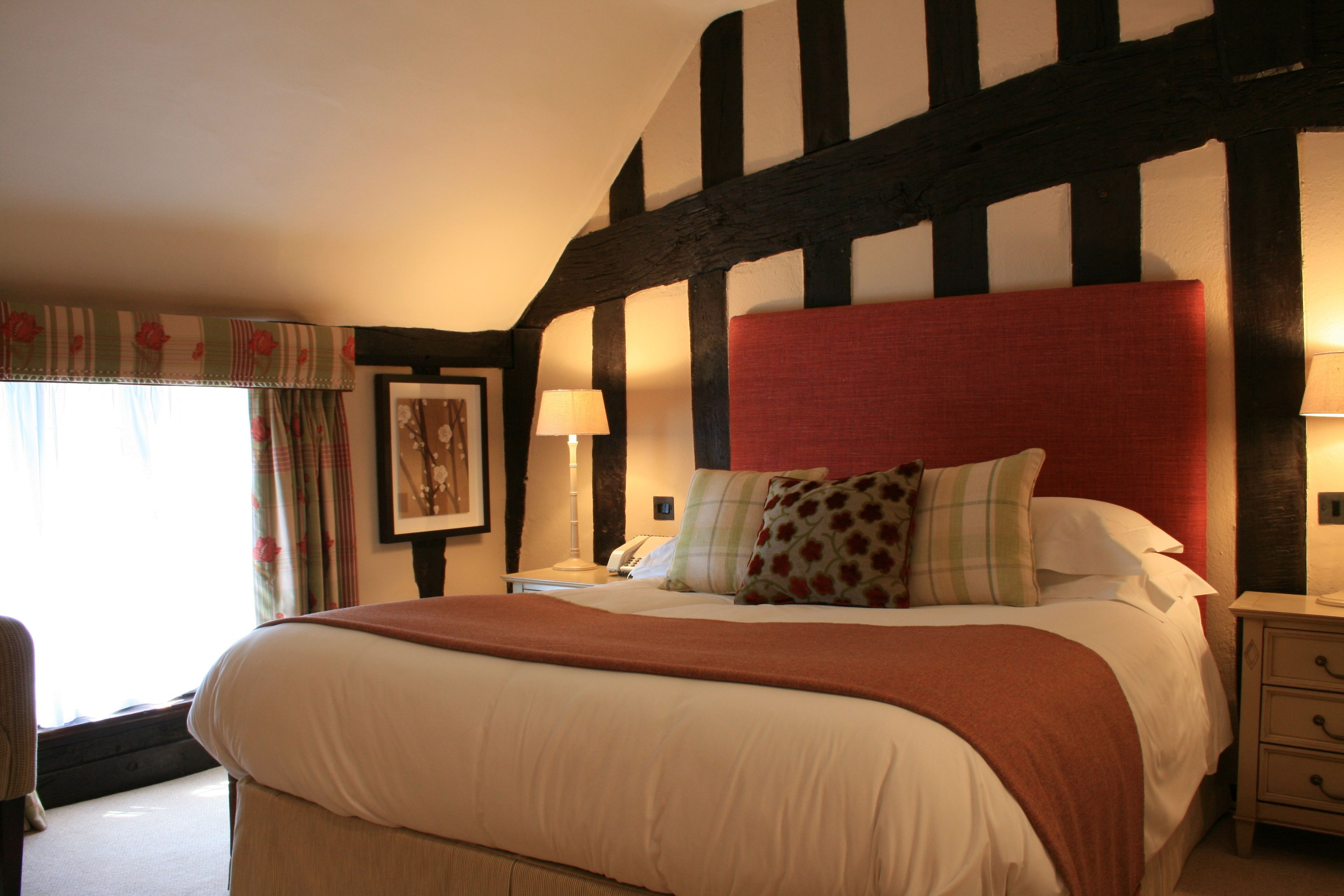 Une chambre à coucher avec un grand lit, une table de chevet avec une lampe, un plafond en bois et une fenêtre avec des rideaux.