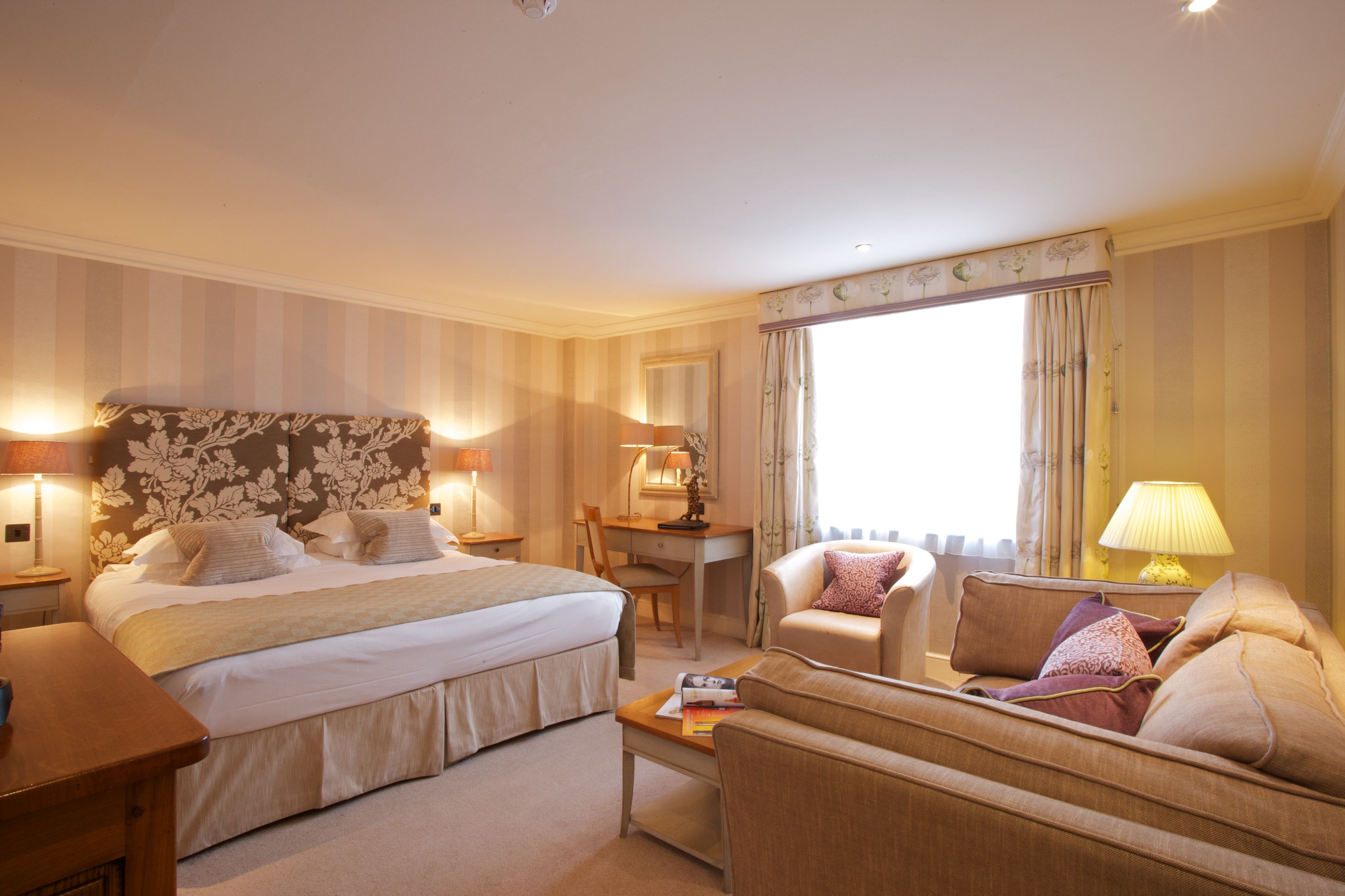 Une chambre d’hôtel avec un grand lit, un bureau, une chaise, un canapé et une fenêtre avec des rideaux.