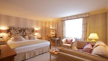 Une chambre d’hôtel avec un grand lit, un bureau, une chaise, un canapé et une fenêtre avec des rideaux.