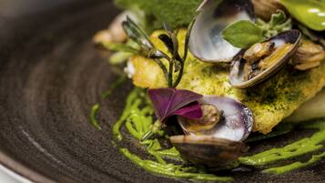 A dish with clams and greens on a dark plate.