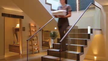 A modern staircase with wooden steps and glass railings, leading to a landing area with a plant and a ladder.