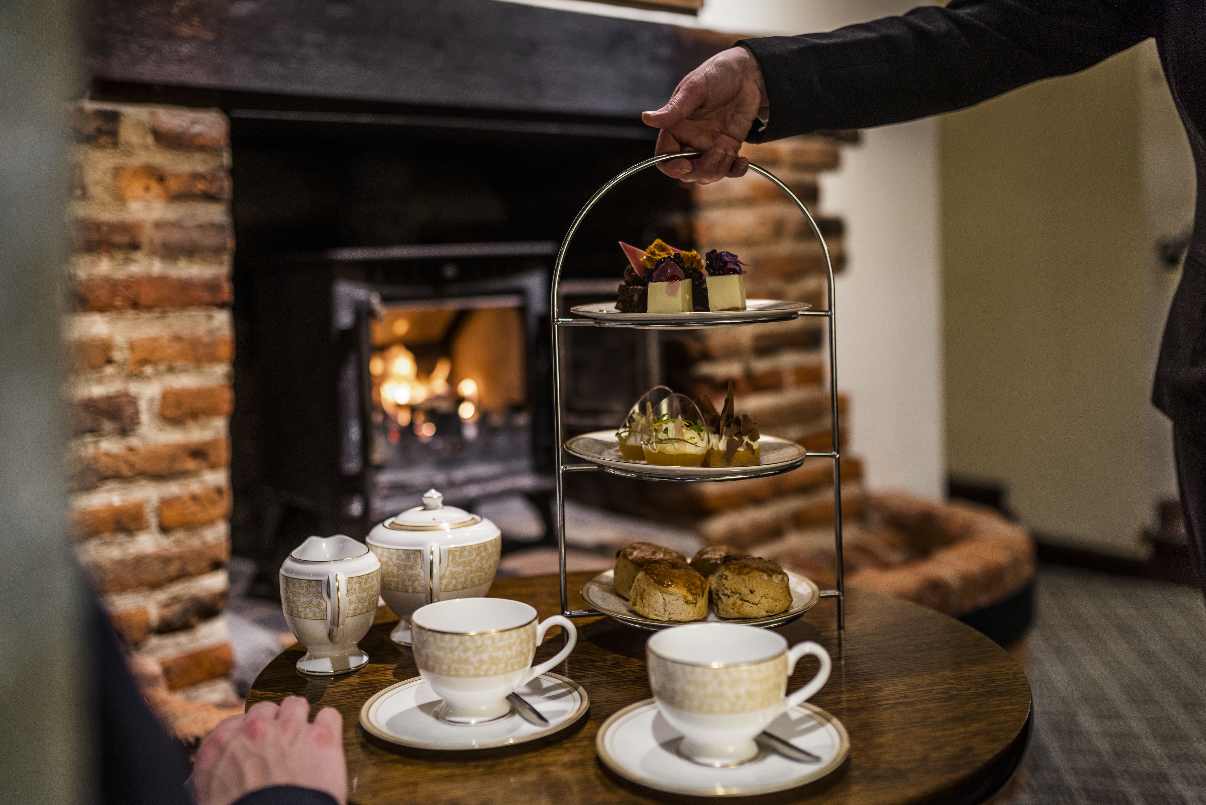 A three-tiered dessert stand with pastries and a tea set on a round table.