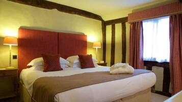 A hotel room with a large bed, two bedside lamps, a window with checkered curtains, and a wooden ceiling beam.