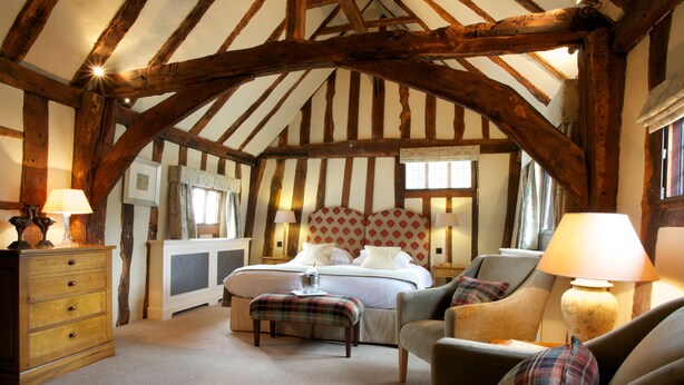 A room with exposed wooden beams, a bed with a headboard, a sofa, a chair, a wooden dresser, and a lamp. - The Swan Hotel (Sudbury)