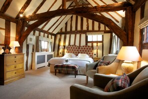 A room with exposed wooden beams, a bed with a headboard, a sofa, a chair, a wooden dresser, and a lamp. - The Swan Hotel (Sudbury)