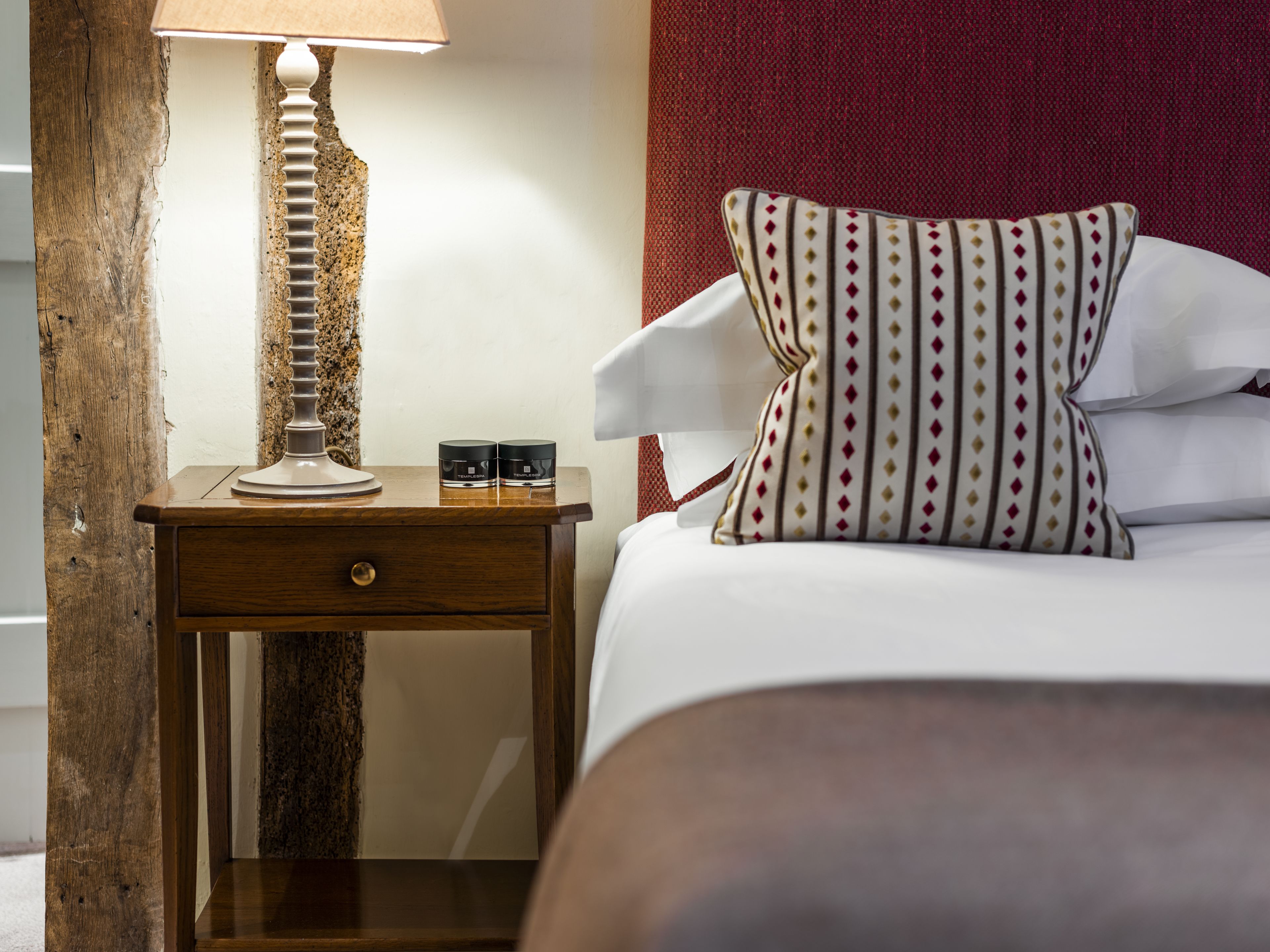 A neatly made bed with striped pillows, a wooden nightstand with a lamp, and two small containers on the nightstand.
