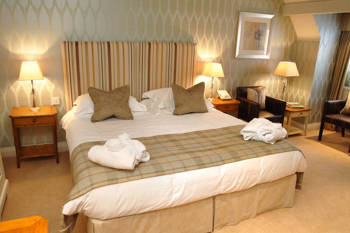 A neatly made bed with pillows, a bedside table with a lamp, and a chair in a hotel room.