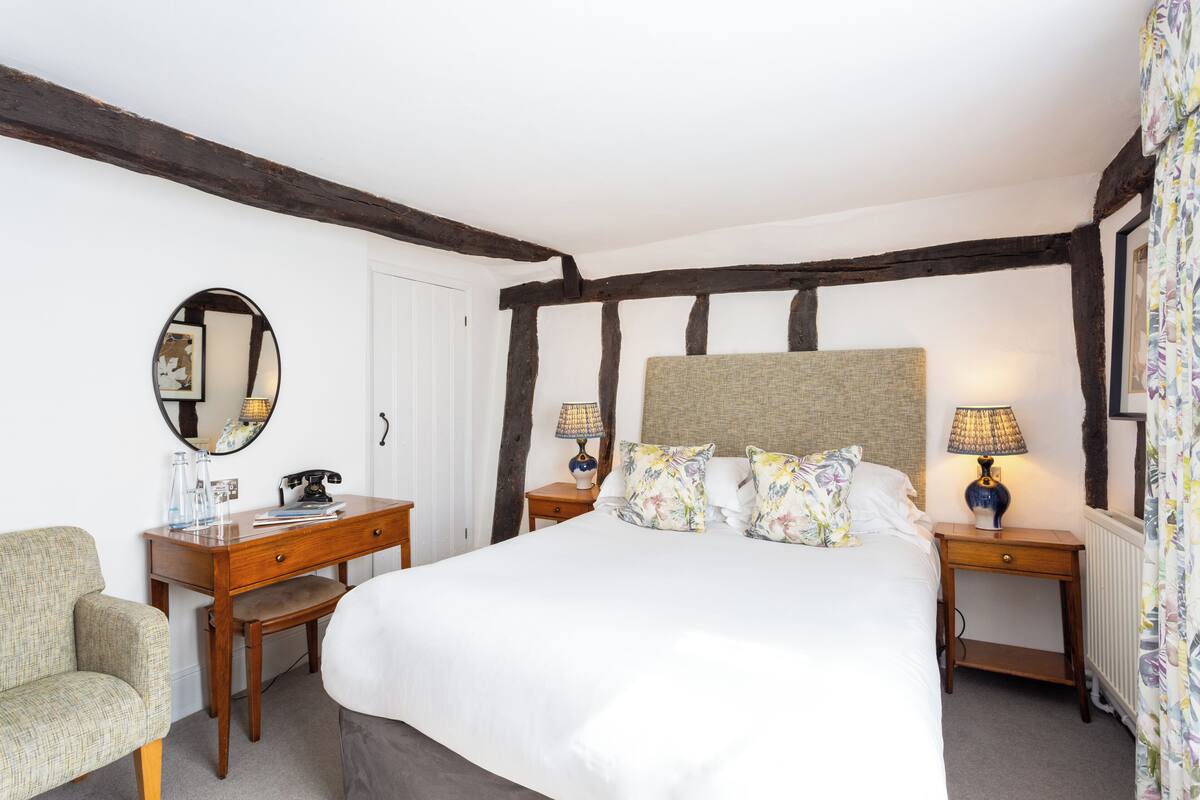 A bedroom with a large bed, wooden nightstands, a chair, a mirror, and a dresser.
