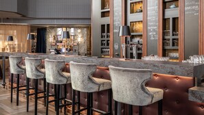 Eine Bar mit hohen Hockern, einer Marmorplatte und Regalen mit Gläsern.