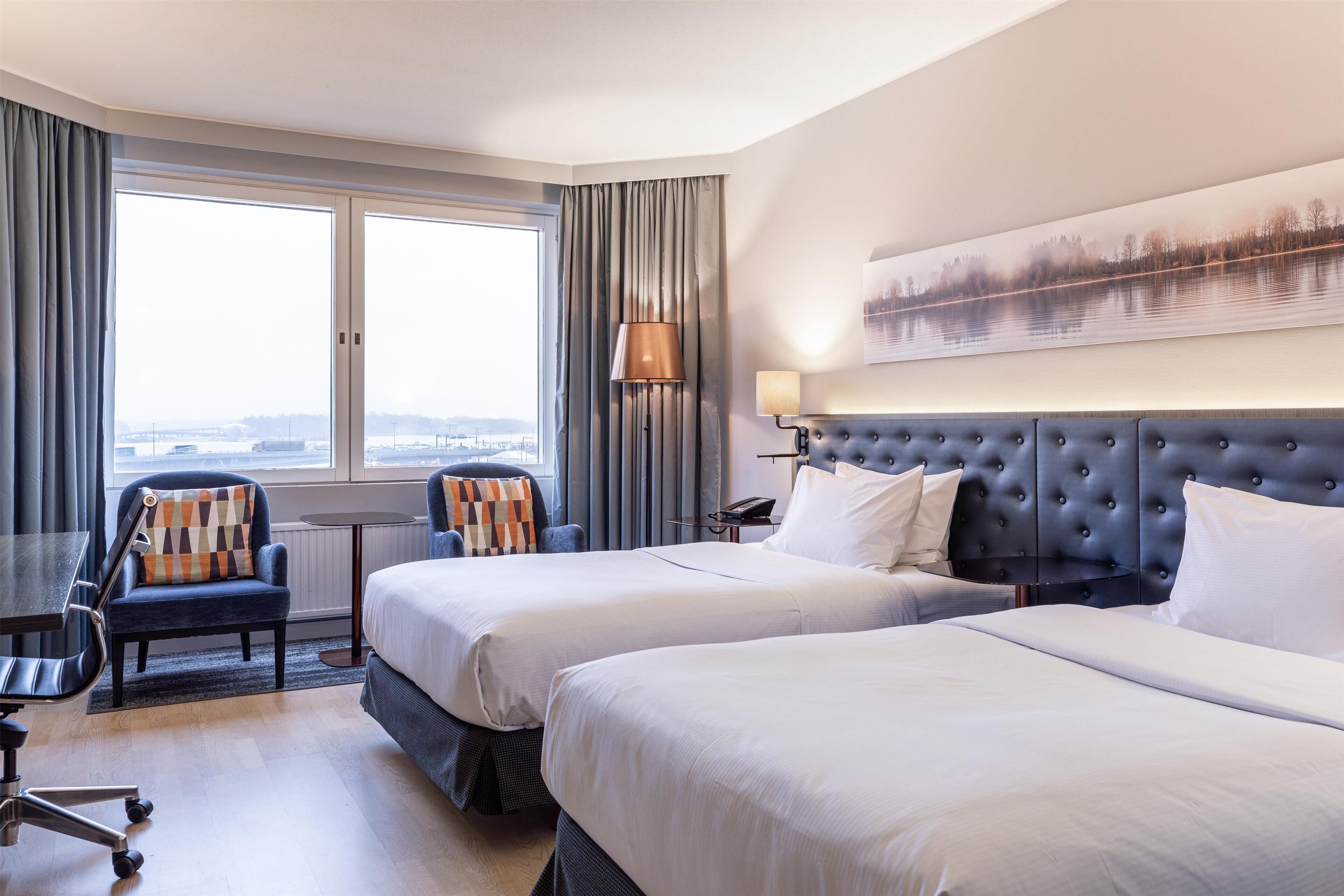 Une chambre d’hôtel avec deux lits, un bureau, une chaise, une lampe et une vue sur un lac.