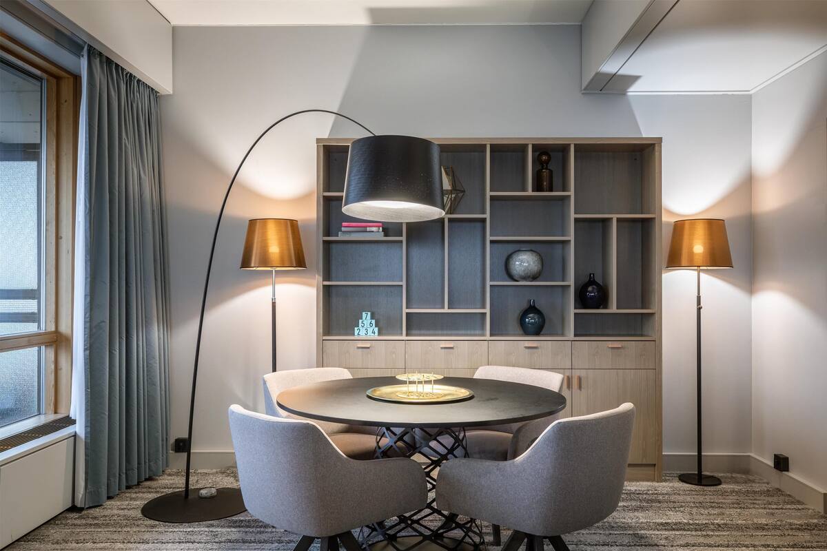A modern dining area with a round table, two chairs, and a bookshelf in the background.