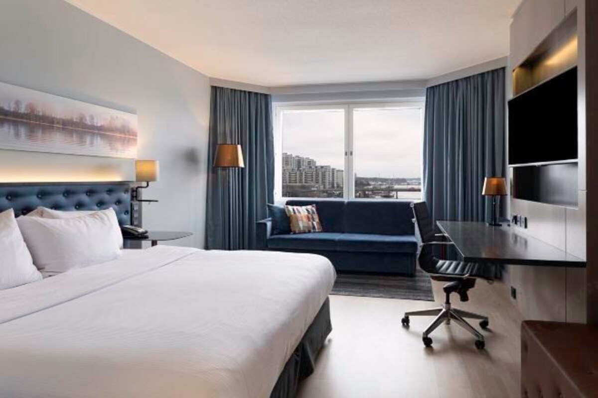 Habitación de hotel con una cama grande, un escritorio, una silla, un sofá y un televisor.