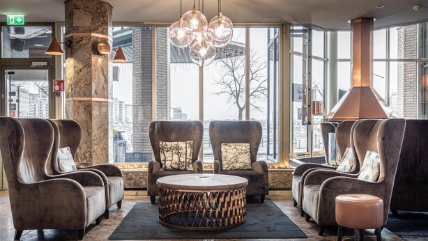 Eine Lobby mit Ledersesseln, einem runden Couchtisch und einem großen Fenster mit Blick auf die Stadt.