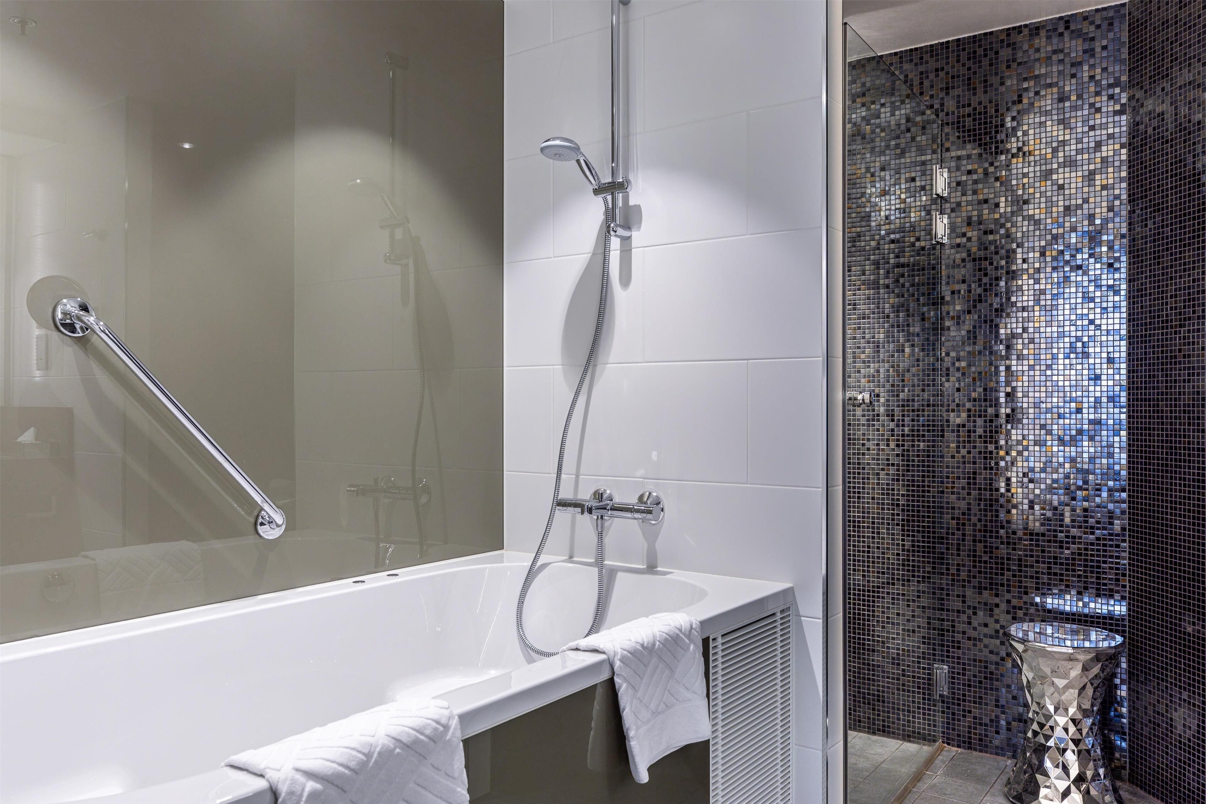 Un baño moderno con ducha de vidrio, una bañera independiente y un revestimiento de mosaicos.